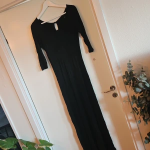 Svart långklänning med trekvarts armar  - Elegant svart långklänning med trekvarts armar och en stilren design. Klänningen har en liten öppning baktill som ger en extra touch. Perfekt för en stilfull look.