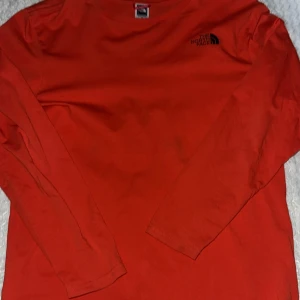 Röd långärmad tröja från The North Face - Säljer en röd långärmad tröja från The North Face med logga på bröstet och ryggen. Perfekt för en casual look eller lager på lager under kallare dagar. Tröjan är tillverkad i ett mjukt och bekvämt material.