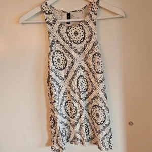 Mönstrad ärmlös topp från H&M - Säljer en stilren ärmlös topp från H&M med ett svart och vitt mönster. Perfekt för varma dagar eller som ett lager under en jacka. Toppen har en rund halsringning och är tillverkad i ett mjukt material.