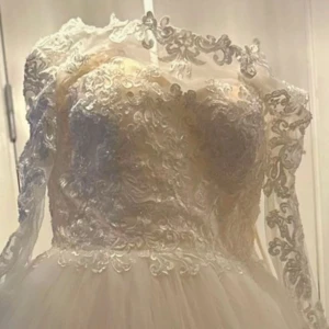 Vit spetsklänning med lång ärm - Elegant vit klänning med vacker spetsdetaljering och lång ärm. Klänningen har en romantisk känsla med sin långa längd och detaljerade spetsmönster. Perfekt för speciella tillfällen.