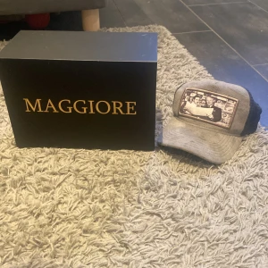 Grå keps från Maggiore - Snygg grå keps från Maggiore med ett unikt tryck framtill. Kepsen har ett justerbart spänne baktill och meshmaterial för bra ventilation. Perfekt för en avslappnad stil.