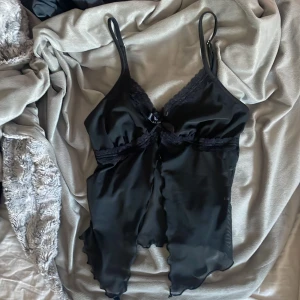 Svart satinlinne med spetsdetaljer - snyggt svart satinlinne med spetsdetaljer och justerbara axelband. linnet har en söt rosett framtill och en  v-ringning. knappt använd