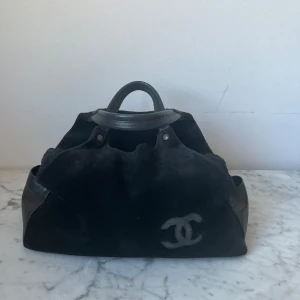 Svart handväska med logotyp - Snygg svart handväska  i mocka med skinn detaljer. Väskan har dubbla handtag och en dragkedja på baksidan. Inte en chanelväska!!!