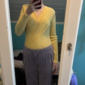 Gul omlottopp - Säljer en snygg gul omlottopp med ribbad struktur. Toppen har långa ärmar och en v-ringad design som ger en stilren look. Perfekt för att liva upp garderoben med lite färg!