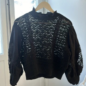 Svart spetsblus - Snygg svart blus med spetsdetaljer och långa ärmar. Perfekt för en stilren look med en touch av elegans. Blusen har en hög krage och elastiska muddar vid ärmsluten.