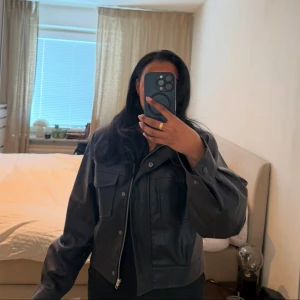 Svart PU-jacka från Josefine HJ - Snygg svart PU-jacka från Josefine HJ med dragkedja och stora fickor framtill. Jackan har en modern look med en hög krage och långa ärmar. Perfekt för en stilren outfit. Köpt för 999kr