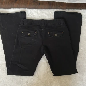 Svarta låg midjade bootcut byxor - Snygga svarta bootcut byxor med dekorativa knappar på fickorna. I storlek 34.
