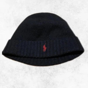 Mössa från Polo Ralph Lauren  - Snygg svart mössa från Polo Ralph Lauren med röd broderad logga framtill. Perfekt för att hålla värmen under kyliga dagar. Klassisk design som passar till det mesta.