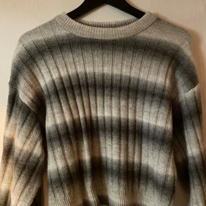 Grå och svart ribbad tröja - Säljer en stilren grå och svart ribbad tröja med långa ärmar. Perfekt för kyligare dagar med sitt mjuka material och klassiska design. Passar bra till både jeans och kjol.