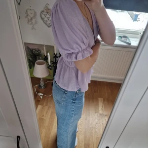 Ljuslila blus med knytband - Säljer en söt ljuslila blus med knytband i midjan och puffiga kortärmar. Blusen har en v-ringad design och är perfekt för vår och sommar. Den är tillverkad i ett lätt och luftigt material. Helt oanvänd o köpt från gina💗🌸