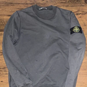 Grå sweatshirt från Stone Island - Säljer en stilren grå sweatshirt från Stone Island med deras ikoniska märke på ärmen. Storlek M. Tröjan har långa ärmar och en rund halsringning. Perfekt för en avslappnad och trendig look. Nu pris kostar den 3000 
