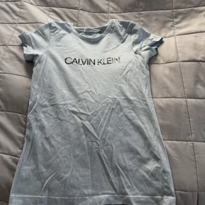 Ljusblå t-shirt från Calvin Klein - Säljer en ljusblå t-shirt från Calvin Klein med korta ärmar och tryck framtill. T-shirten har en klassisk rund halsringning och är gjord i mjukt material. ( använd 1 gång)