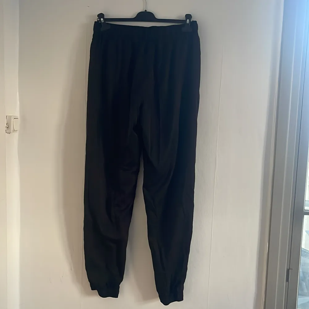 Säljer ett par svarta träningsbyxor från Puma med elastisk midja och logga på benet. Perfekta för en avslappnad stil. Tillverkade i ett mjukt och bekvämt material.. Farkut & Housut.