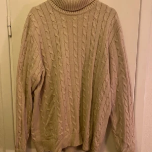 Beige stickad polotröja - Säljer en mysig beige stickad polotröja med kabelstickat mönster. Perfekt för kyliga dagar med sin höga krage och långa ärmar. Tröjan har en klassisk och tidlös design som passar till det mesta. Ett måste i garderoben för den som älskar stil och komfort.