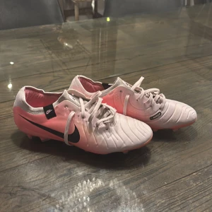 Nike Tiempo - Snygga Nike Tiempo i en gradient av rosa och vit med svart Nike-logga. Skorna är inte använda så mycket och skorna har snörning och är designade för optimal bollkontroll. Perfekta för fotbollsplanen!