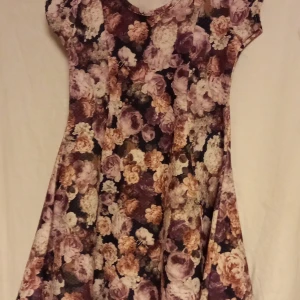 Blommig klänning från Bebe Lonia - Charmig blommig klänning från Bebe Lonia i härliga nyanser av lila och beige. Klänningen har korta ärmar och ett vackert blommönster som ger en romantisk känsla. Perfekt för små fashionistas som älskar att klä upp sig!