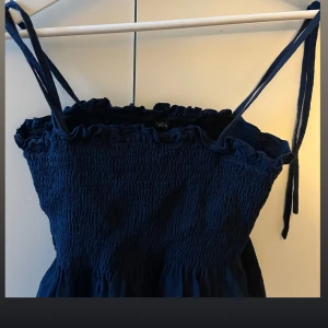 Marinblå topp med smockdetaljer - Säljer en marinblå klänning med smockdetaljer och smala axelband. Perfekt för sommarens varma dagar. Klänningen har en söt volangkant upptill som ger en romantisk touch. Skriv vid flera frågor eller vid intresse 💞