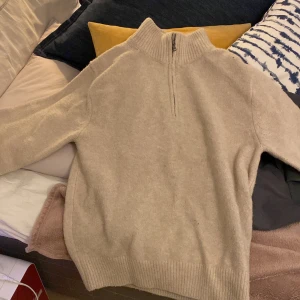 Beige stickad tröja från Uniqlo - Säljer en mysig beige stickad tröja från Uniqlo. Tröjan har en halv dragkedja vid halsen och ribbstickade muddar vid ärmslut och nederkant. Perfekt för kyliga dagar! Riktigt skön tröja som är varm och hade rekommenderat att ha den när man kommer tillbaka från skidbacken eller om man bara vill värma sig. 