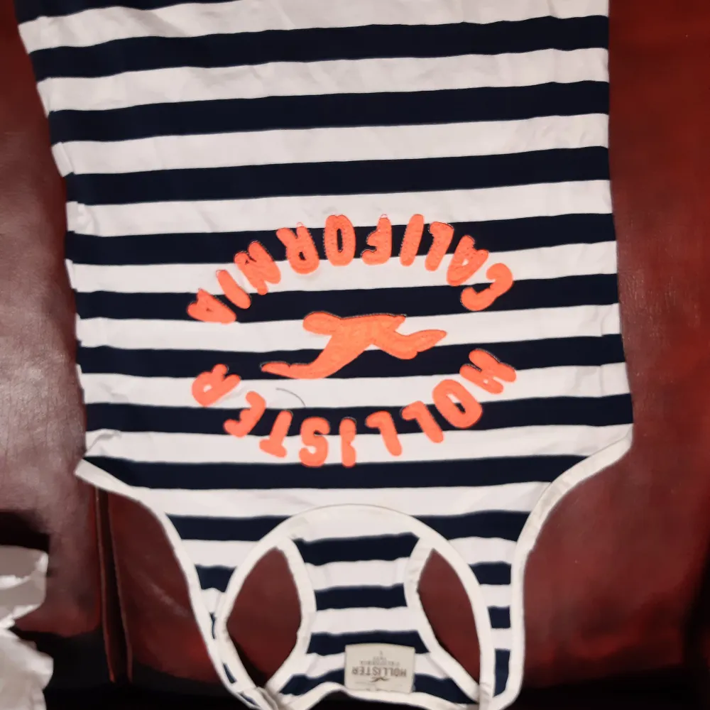 Säljer en randig linnetopp från Hollister i marinblått och vitt med orange text och logga på framsidan. Perfekt för en avslappnad stil.. Yläosat.