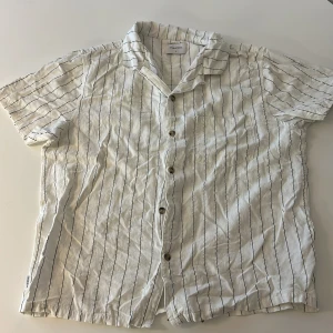 Vit och svart randig skjorta från Stayhard - Snygg vit skjorta med svarta ränder från Stayhard. Kortärmad design med knappar framtill. Perfekt för en avslappnad stil. Tillverkad i ett lätt och bekvämt material.