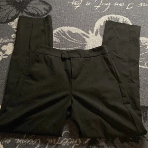 Svarta kostymbyxor från Gina Tricot - Snygga svarta kostymbyxor från Gina Tricot i storlek XS. Byxorna har en stilren design med dragkedja och knapp framtill. Perfekta för en chic och elegant look.