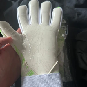 Fotbollshandskar från One - Snygga fotbollshandskar från One med ett coolt geometriskt mönster i grönt och vitt. Handskarna har en bred handledsrem för extra stöd och komfort. Perfekta för målvakter som vill ha både stil och funktion på planen. Oöppnade, säljs pågrund av jag skadat mig så de ej blir fotboll denna säsongen 