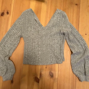 Grå ribbad tröja från Shein - Säljer en snygg grå ribbad tröja från Shein med v-ringning och långa ärmar. Tröjan är croppad och har en stilren design som passar perfekt till olika outfits. Perfekt för både höst och vår!