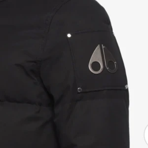 Svart pufferjacka med pälsdetaljer - Säljer en svart pufferjacka från Moose Knuckles med pälsdetaljer på huvan. Jackan har dragkedja och knappar framtill samt flera praktiska fickor. Perfekt för kalla vinterdagar. Jackan är i storlek xl i barnstorlek/xs i vuxenstorlek 