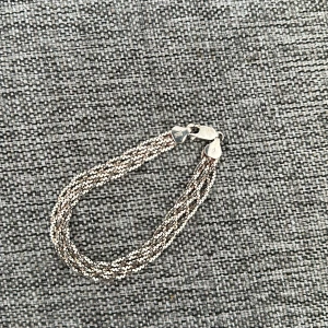 Flätat silverarmband - Elegant flätat armband i silver med flera tunna kedjor som ger en glittrig effekt. Perfekt för att lägga till en touch av stil till din outfit. Armbandet har en säker låsning och mäter cirka 18 cm i längd.