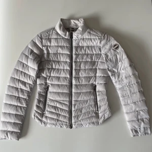 Vit dunjacka från Colmar - Pris kan diskuteras! Säljer en stilren vit dunjacka från Colmar med dragkedja och hög krage. Jackan har en quiltad design och två praktiska fickor med dragkedjor. Perfekt för kyligare dagar och ger en snygg look.