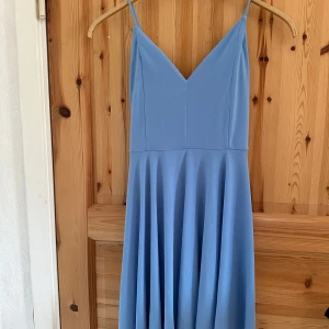 Blå klänning med v-ringning - Säljer en elegant blå klänning från Bikbok med v-ringning och smala axelband. Klänningen har en flödande kjol och är perfekt för sommarens tillfällen. Den är tillverkad i ett mjukt och bekvämt material.