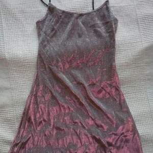 Glittrig klänning med tunna axelband - Säljer en glittrig klänning med tunna axelband. Klänningen har en skimrande yta i en mörk ton med inslag av rosa. Perfekt för en festlig kväll! ✨