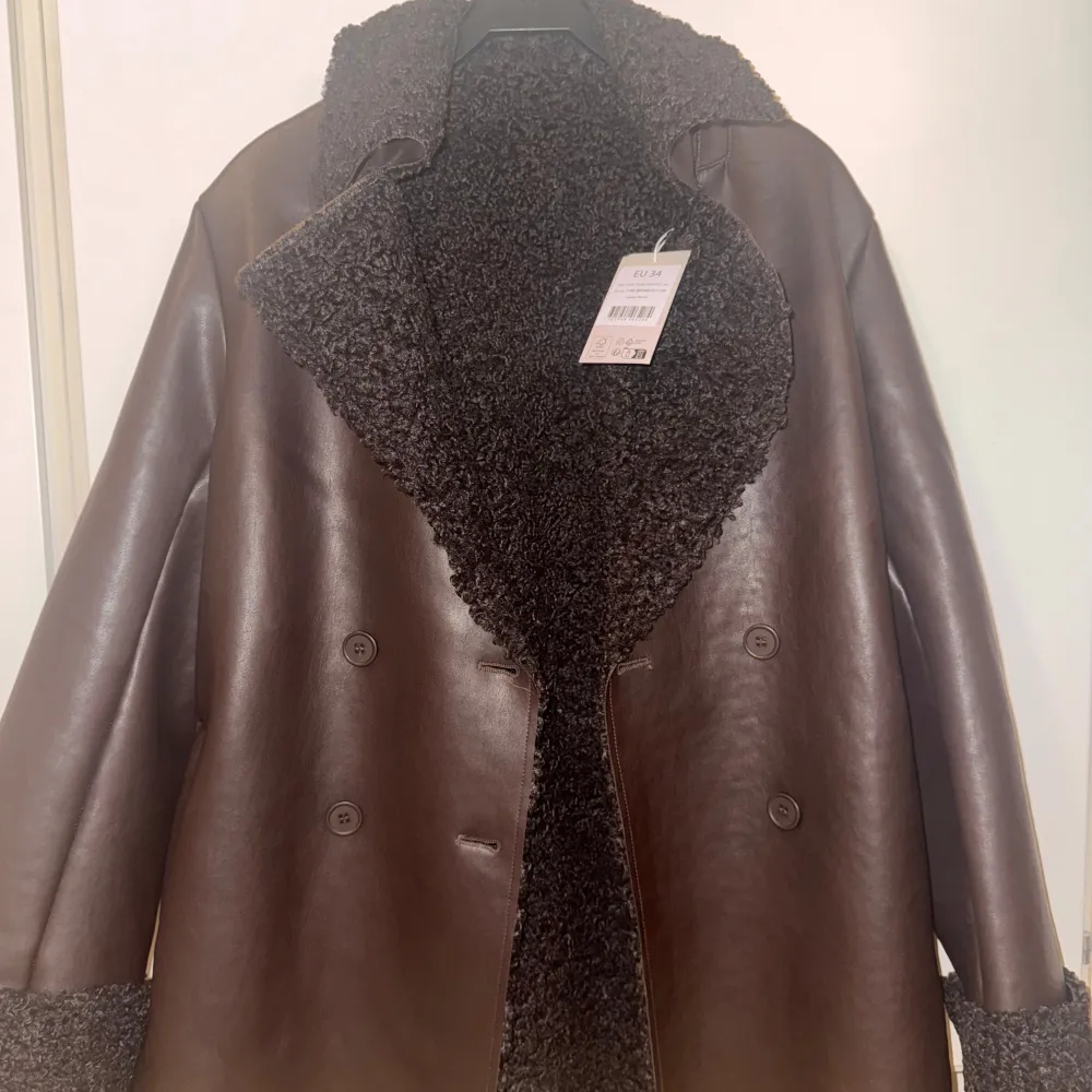 Brun kappa från NA-KD som aldrig använd. Endast testad. Lappen är kvar. Kappan är i PU och materialet på insidan är teddy-material. Skärpet går att ta av. Nypris 1199 kr.. Takit.