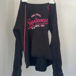 Svart långärmad tröja från SOC - Säljer en svart långärmad tröja från SOC med rosa detaljer och texten 'Sportswear' på framsidan. Tröjan har ribbad hals och är perfekt för en sportig look. Passar bra för kyligare dagar.