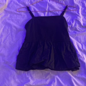 Svart ärmlös topp - Säljer en stilren svart ärmlös topp med volangdetaljer. Toppen har smala axelband och en luftig passform. Lapen i ryggen är borta men den är från HM. Kontakta för mer 🤍