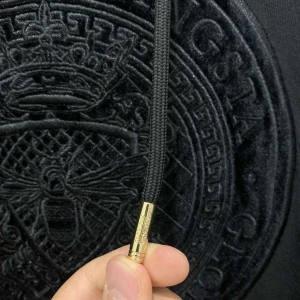 Svart hoodie från Glorious Gangsta - Snygg svart hoodie från Glorious Gangsta med ett stort, broderat emblem på bröstet. Den har guldfärgade detaljer på snörena och ett mönster längs ärmarna. Perfekt för en stilren look ingen skador absolut 