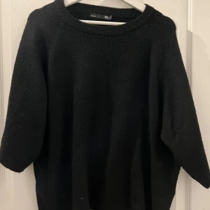 Svart stickad tröja från 157 - Säljer en svart oversized stickad tröja från 157. Tröjan har en enkel design med ribbstickad halsringning och trekvartsärmar. Perfekt för en stilren och bekväm look.