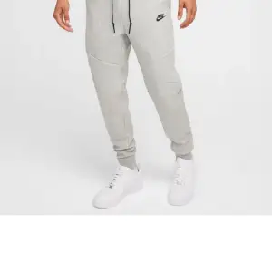 Snygga grå mjukisbyxor från Nike med svart logga på låret. Byxorna har en bekväm passform med snörning i midjan och muddar vid bensluten. Perfekta för en avslappnad stil.
