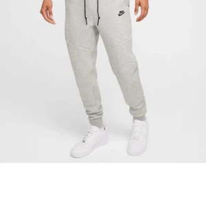 Grå mjukisbyxor från Nike - Snygga grå mjukisbyxor från Nike med svart logga på låret. Byxorna har en bekväm passform med snörning i midjan och muddar vid bensluten. Perfekta för en avslappnad stil.