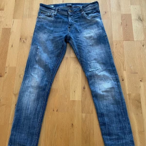 Blå jeansbyxor med slitningar - Snygga jeans från Jack and Jones, modellen heter slim fit/glenn. Storleken är W 29 och 32 i längd. Fina slitningar som ger en äldre look. 