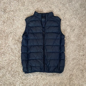 Mörkblå dunväst från Lawrence Grey - Säljer en stilren mörkblå dunväst från Lawrence Grey. Västen har en dragkedja framtill och är perfekt för både kyligare dagar men även som ett extra lager under varmare dagar. Den är lätt och smidig att bära, vilket gör den till ett mångsidigt plagg i garderoben. Har diskrete fickor men kjedja på sidorna. Storlek L men passar också M Postas antigen samma dag som köp eller dagen därpå💯🙌
