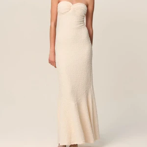 Adoore rio klänning - Elegant champagnefärgad långklänning med en axelbandslös design och en twistdetalj framtill. Klänningen har en texturerad yta som ger en unik look. Perfekt för speciella tillfällen. Oanvänd med prislapp