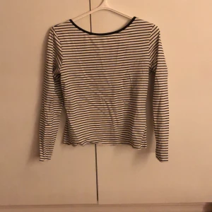 Randig långärmad topp från Lindex - Säljer en stilren randig topp från Lindex i svart och vitt. Den har långa ärmar och en rund halsringning med svart kant. Den går även lite lägre i ryggen, inte jättemycket men lite. Man ser inte bh- banden i ryggen när man har den på sig. Verkligen så snygg. Perfekt för en avslappnad men ändå snygg look.😍😍