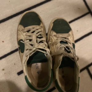 Vita och gröna sneakers med klöverdetalj - Snygga vita sneakers med gröna detaljer och en unik klöverdesign på sidan. Skorna har snörning och en klassisk siluett som passar perfekt för en avslappnad stil. Perfekta för dig som vill ha något annorlunda i garderoben. Med kommer en låda, villl påpeka att de inte går att köpa längre 