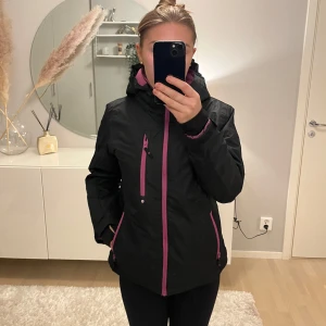 Svart jacka från Everest med rosa detaljer - Säljer en svart jacka från Everest med snygga rosa dragkedjor och detaljer. Jackan har en huva och är perfekt för kyligare dagar. Den har en praktisk dragkedja framtill och flera fickor för förvaring. Passar perfekt för höst och vinter!