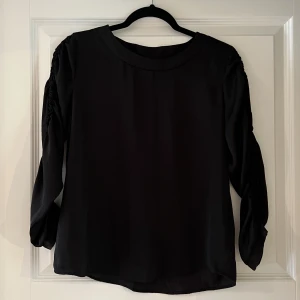 Svart blus JaquelinedeYong - En svart blus i storlek 34 från JaquelinedeYong. Räfflad detalj på ärmarna.