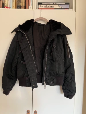 Svart Bomberjacka från Allsaints - Svart jacka från All Saints i storlek Small. Några små fläckar som går att tvätta bort, annars bra skick! Det går att ändra på luvans utseende med hjälp av blixtlåset!