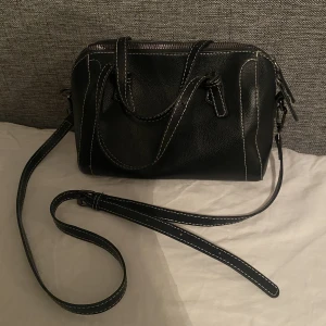Väska - Supersnygg liten svart väska med vita sömmar, nyskick! Väldigt rymlig för sin storlek, både korta och ett långt band.