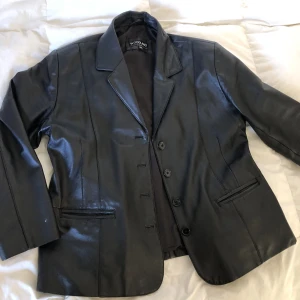 Läderjacka dam 46 - Svart läderjacka/kavaj i mycket gott skick. Äkta vintage läder den Woodland. Storlek UK 22 men passar mer som en 44/46. Byst: 120cm. Siden foder på insidan, annars 100% äkta läder. Finns inga bilder på men Dma gärna vid andra frågor eller funderingar. 