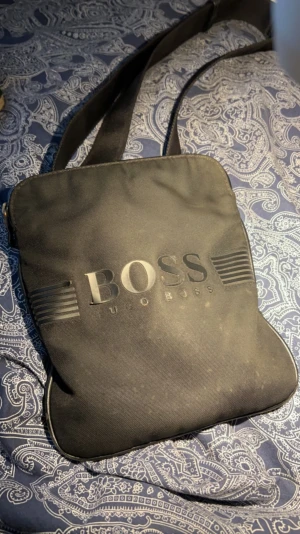 Hugboss axelväska  - Säljer en svart hugboss axelväska som jag har haft ett bra tag. Väskan har några små fläckar som går bort genom tvätt. Gummit på framsidan är lite löst men går att limma fast. Priset går att diskutera.